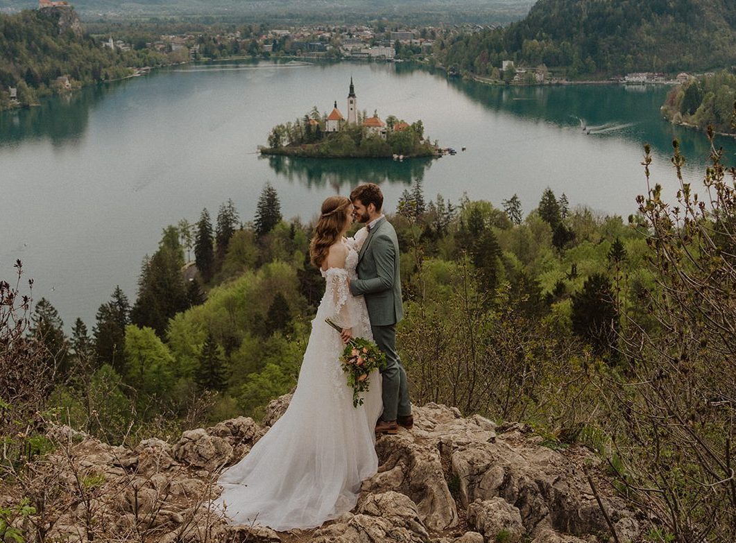 A couple sharing a quiet moment on a rocky viewpoint above Lake Bled, the island church and castle beyond
