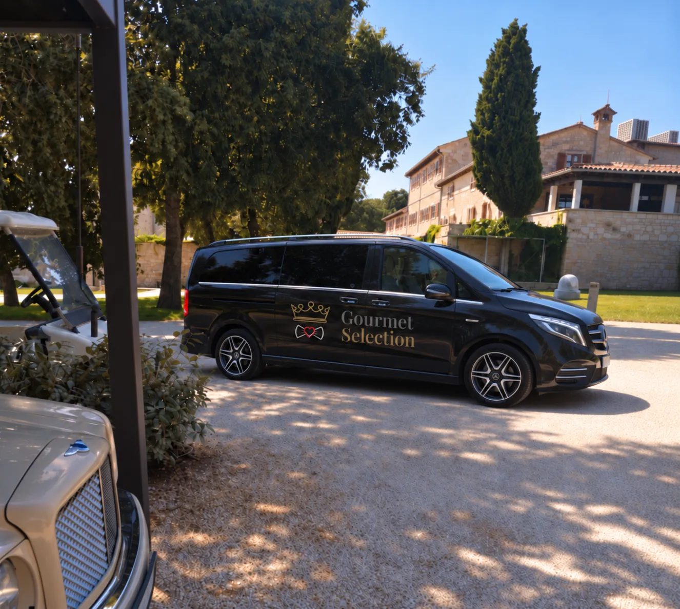 The black Gourmet Selection van with its crown emblem waiting on the gravel of a stone estate courtyard, shaded by old trees