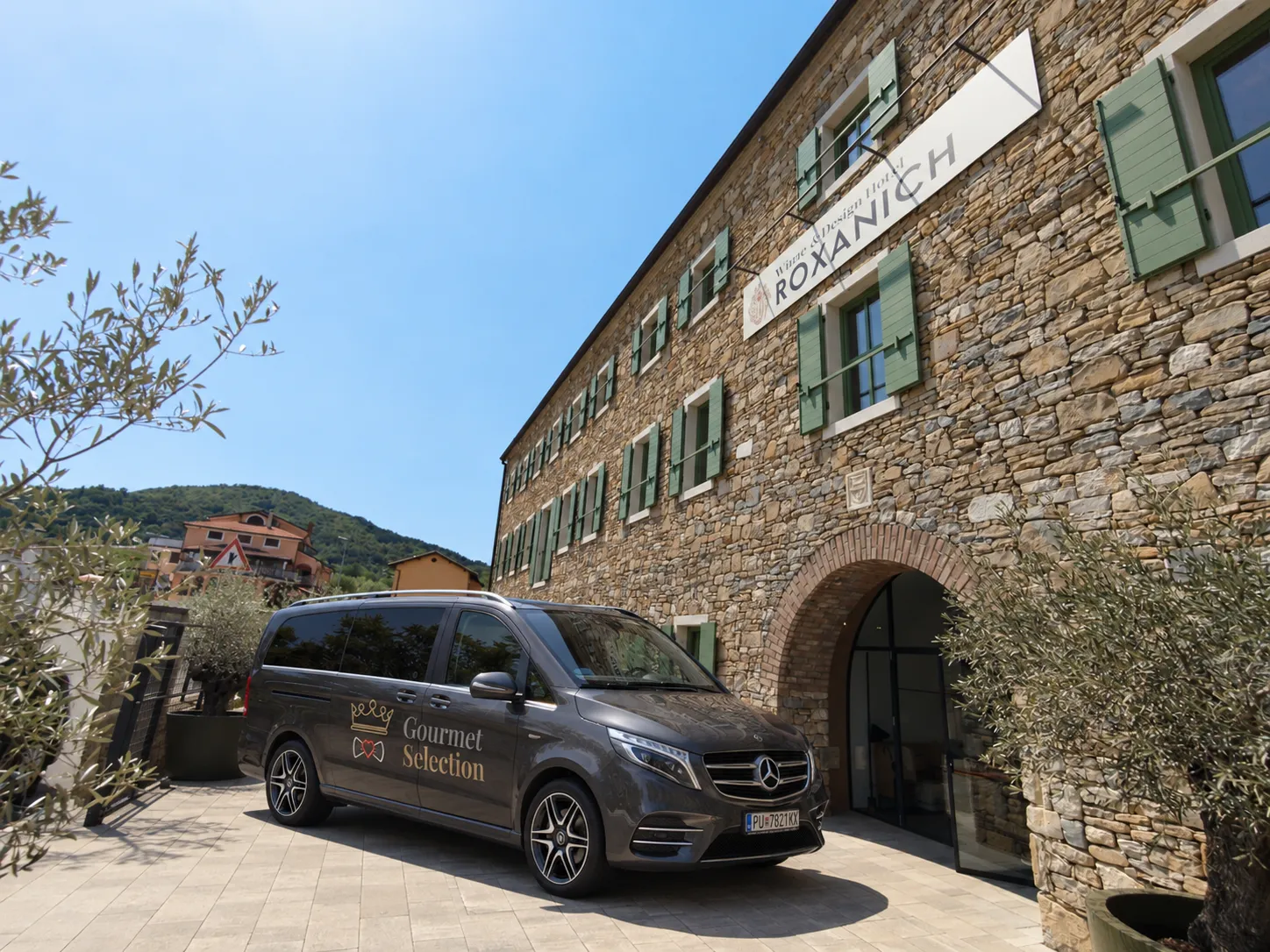 The Gourmet Selection van with its crown emblem parked in front of the long stone facade of a converted winery below Motovun